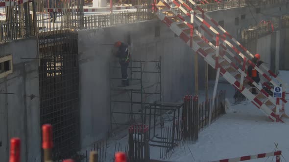 Builder Grinds Wall on Scaffolds at Construction Site