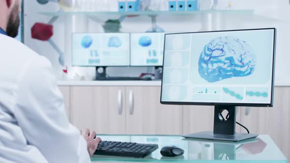 Doctor in His Office Typing on Computer at Modern Glass Desk