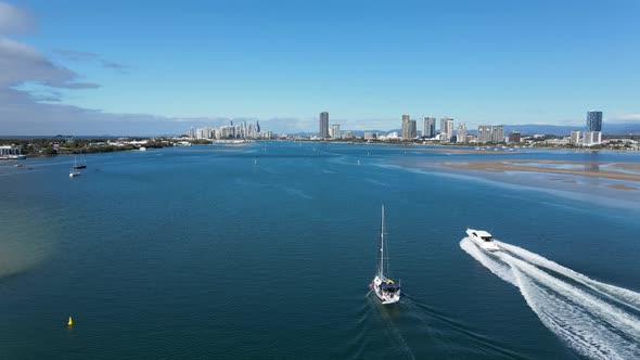 A fasting speed boat glides past a sailing boat as it heads toward a towering skyline of urban spraw