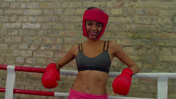 Portrait of Smiling Sporty Black Woman Boxer Leaning on Ropes Inside Boxing Ring