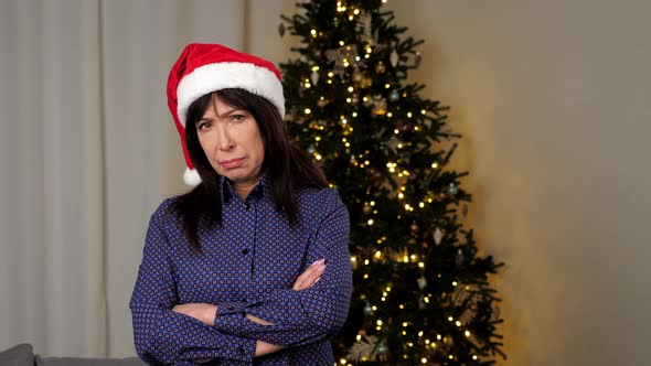 Portrait Upset Aged Woman in Santa Claus Hat Crosses Hands Looks Camera at Home