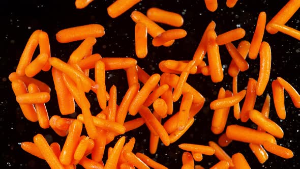 Super Slow Motion Shot of Flying Fresh Baby Carrots and Water Splash Isolated on Black at 1000 Fps