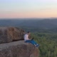 Drone Footage of a Young Man Working on a Laptop Sitting on a Rock Ledge in the Mountains at Sunset - VideoHive Item for Sale
