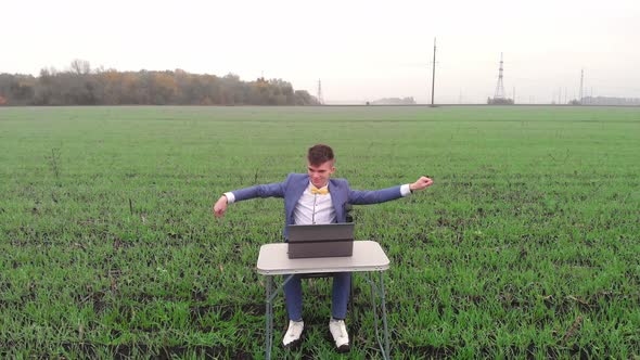 Happy Young Man is Working Outdoor at Spring Field with Laptop and Making Successful Deal or Win