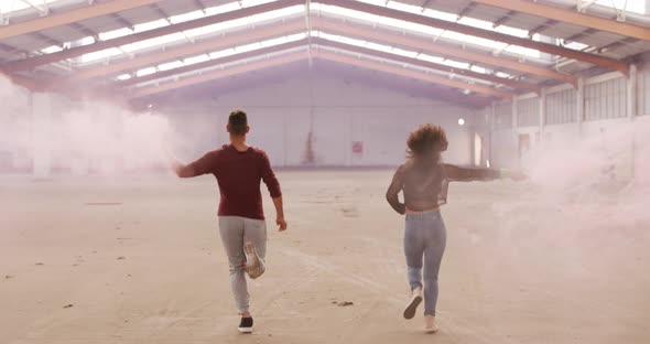 Dancers in an empty warehouse holding smoke grenade