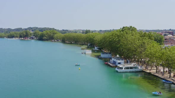 Slow aerial flyby over rowboats and pleasure craft on the shores of Lake Banyoles. Catalonia Spain.