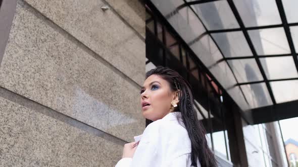 Beautiful Woman in a White Jacket and Blue Top Posing Against the Backdrop of a Building and Windows