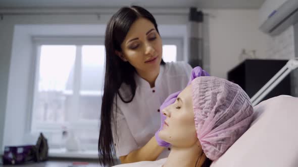 beautiful cosmetologist in a white coat stands over the client and makes Botox