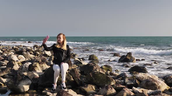 Beautiful Girl Sitting on a Rock By the Sea and Posing for the Camera Taking a Selfie