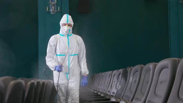 Male Cleaner in Protective Clothes Disinfecting Cinema