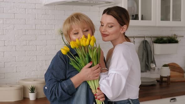 An Elderly Mother with Her Daughter in the Kitchen with Bouquet of Flowers