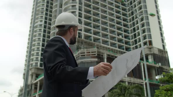 Engineer in White Protective Helmet Checks a Construction Plan in New Microdistrict of the City