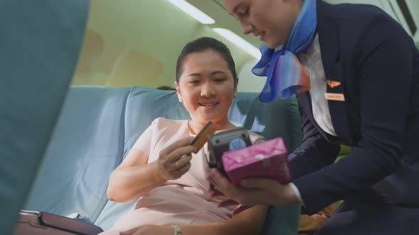 Asian woman sitting in airplane buying onboard product from air hostess and paying by credit card.