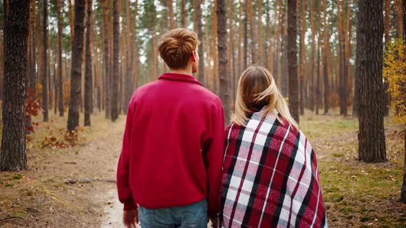 Young Couple Smiling and Talking Holding Hands While Walking By Path in Autumn Wood