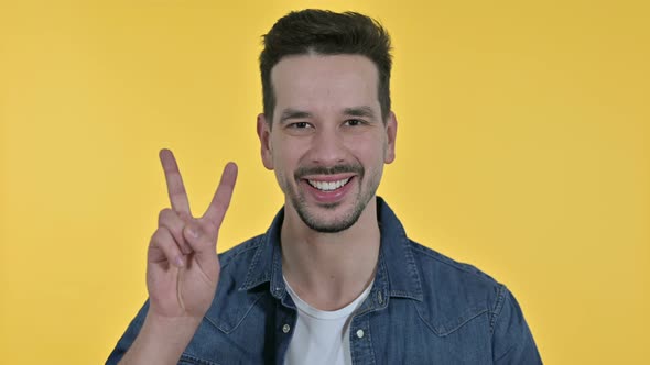 Portrait of Successful Young Businessman Showing Victory Sign, Yellow Background