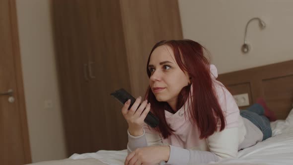 Young Woman Lying on Bed Watching Tv and Laughing