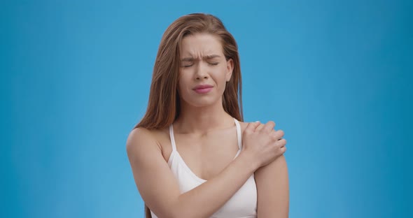 Muscle Pain. Young Woman Suffering From Pain in Shoulder, Blue Studio Background, Slow Motion