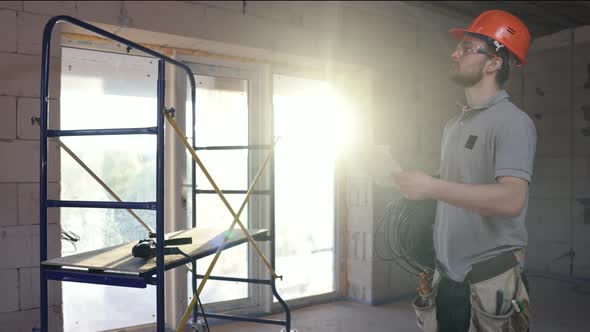 A worker with an electric cable in his hands examines a construction drawing.