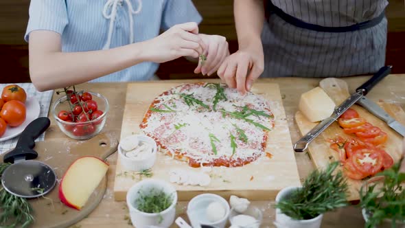 Still shot of two cooks setting toppings on a homemade pizza placed on a wooden cutting board
