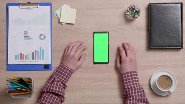 Top View of Male Hands and a Smart Phone with Green Screen on a Wooden Office Desk