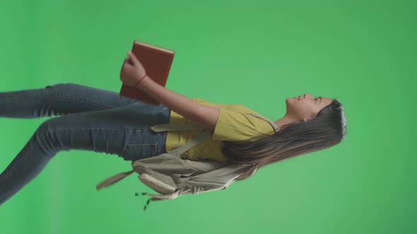 Side View Of Asian Girl Student Holding Book While Walking To School On Green Screen Chroma Key alt