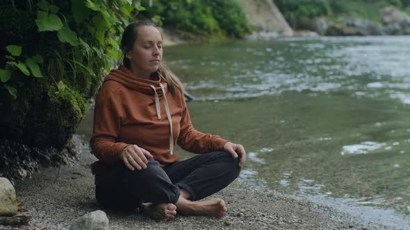Smiling  woman meditates by the mountain river on vacation in nature. Mindful concept