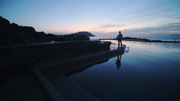 The Profile Of A Man Beside The Swimming Pool Capturing The Sunset In Guernsey. -wide shot