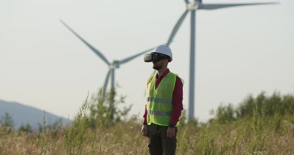 Engineer in VR Glasses Looking at Graphs, Turning Pages. Windmills in the Background