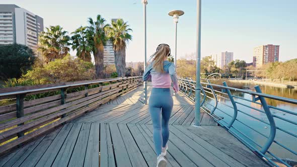 Active Young Lady Runner in Earphones Practice Jogging on Bridge