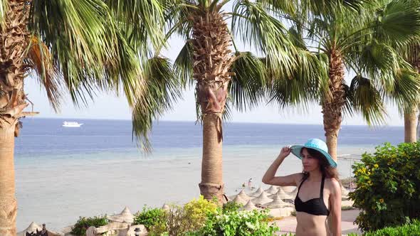 Beautiful Woman Walks on Background of Sea and Palms