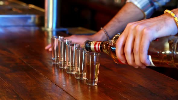 Barman pouring tequila in shot glass at bar counter