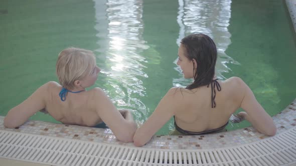 Top View of Positive Caucasian Women Resting at Poolside and Talking. Back View of Young Beautiful