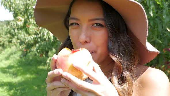 Woman bites into a juicy peach, just picked from the tree.