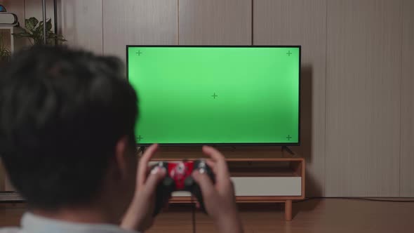 Back View Gamer Using Joystick Playing A Video Game With Green Screen Tv At Home