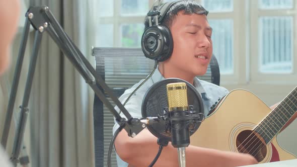 Over Shoulder View, Young Asian Boy Playing The Guitar And Singing While Recording Podcast