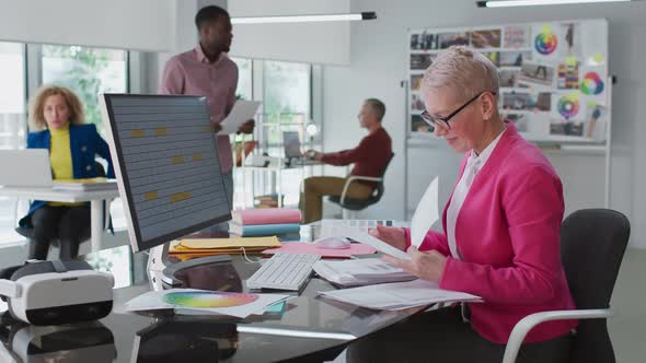 Senior Woman Read Documents Sitting at Desk in Modern Creative Office