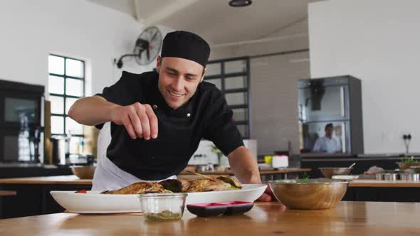 Caucasian male chef preparing a dish and smiling in a kitchen