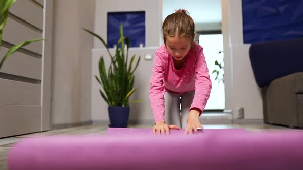 Child, little girl rolling up yoga pilates mat on floor after stretching exercises