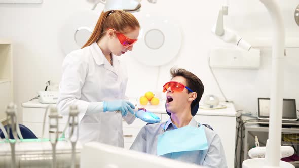 Young Female Dentist in UV Protective Glasses Using Dental Curing Light During Composite Filling