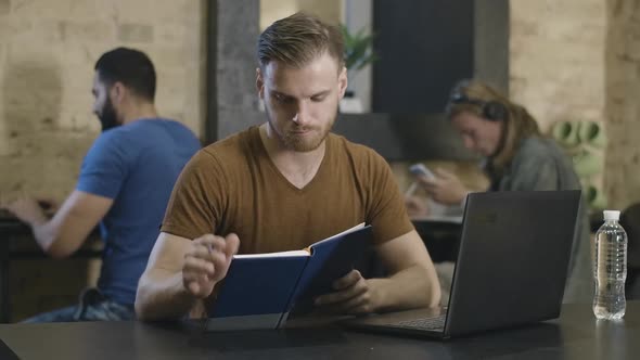 Portrait of Concentrated Caucasian Young Man Working or Studying Online with Blurred Guys Sitting at