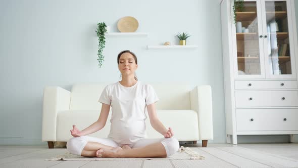 Young Pregnant Lady Meditates Sitting in Padmasana on Floor