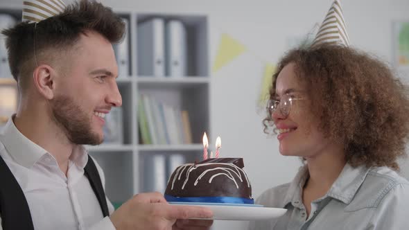 Adorable Couple with Caps on Their Heads Making a Wish and Blowing Out Candles on Birthday Cake