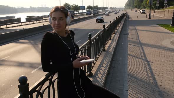 Beautiful Girl in White Headphones Listens To Music Near the Highway. Lifestyle Video of Happy Young