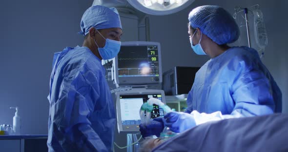 Mixed race surgeons wearing protective clothing looking at heart monitor in operating theatre
