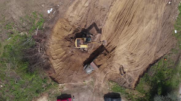 Aerial top view: yellow excavator pouring soil into tipper.