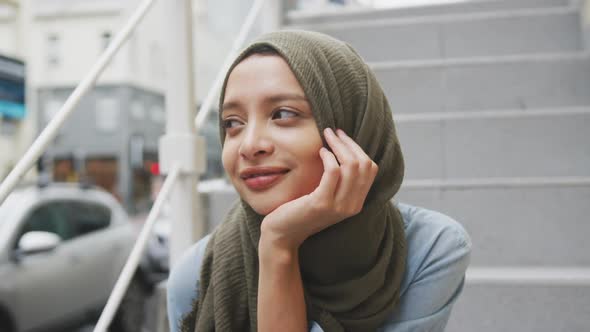 Woman wearing hijab sitting on stairs in the street