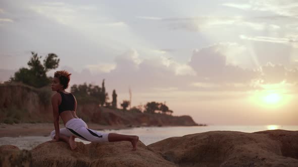 Young Dark Skinned African American Girl Standing in Yoga Asana on Rocks By Sea