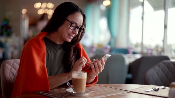 Female Visitor in Restaurant in Lunch Time Drinking Latte and Chatting By Smartphone