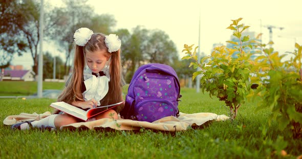 Young Pretty School Girl Reading Book in Park