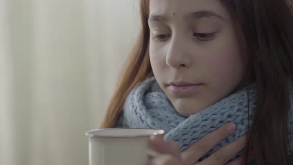 Portrait of Teenage Girl Wrapped in Warm Scarf Holding a Cup of Hot Tea in Hands. The Girl Feels Bad